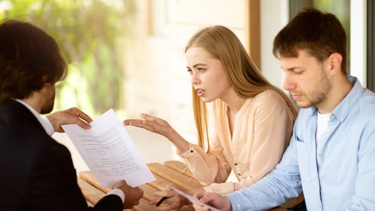 Young married couple upset about property purchase price and real estate agent near house for sale