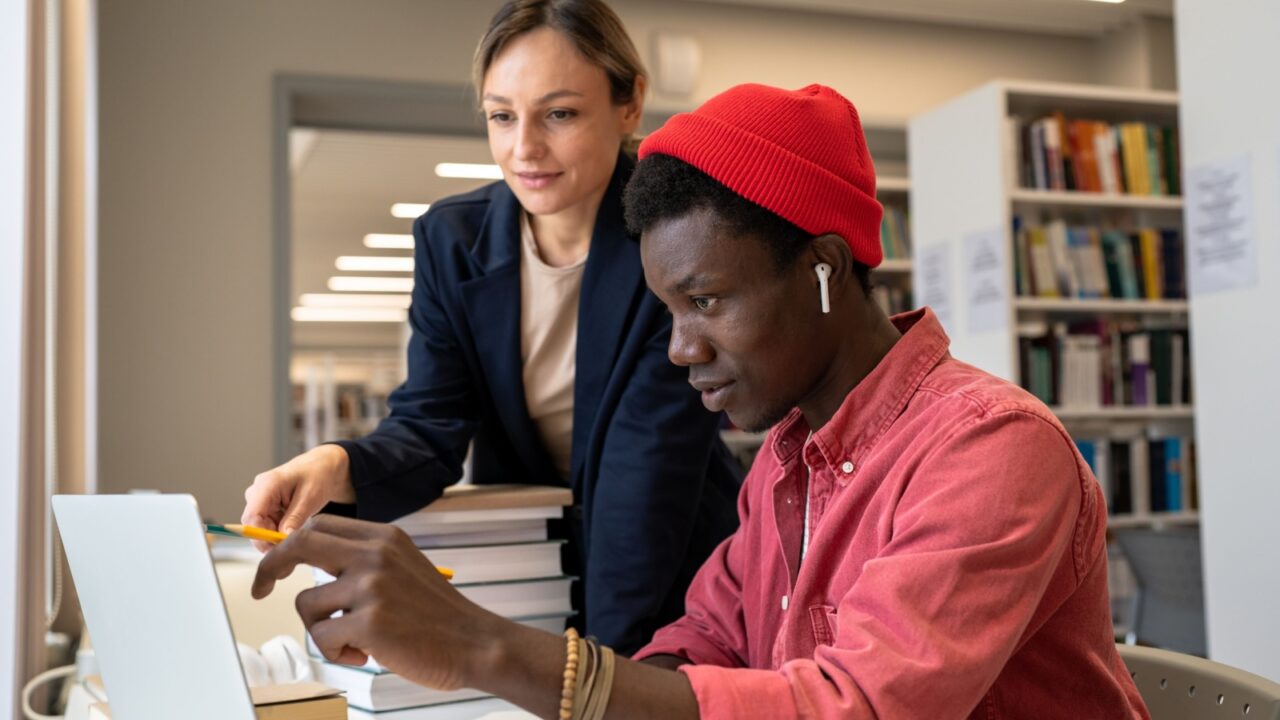 Motivated multiracial concentrated pensive students teammates at university library table discussing study project ideas. Help in preparing test exam from caucasian tutor to African American student.