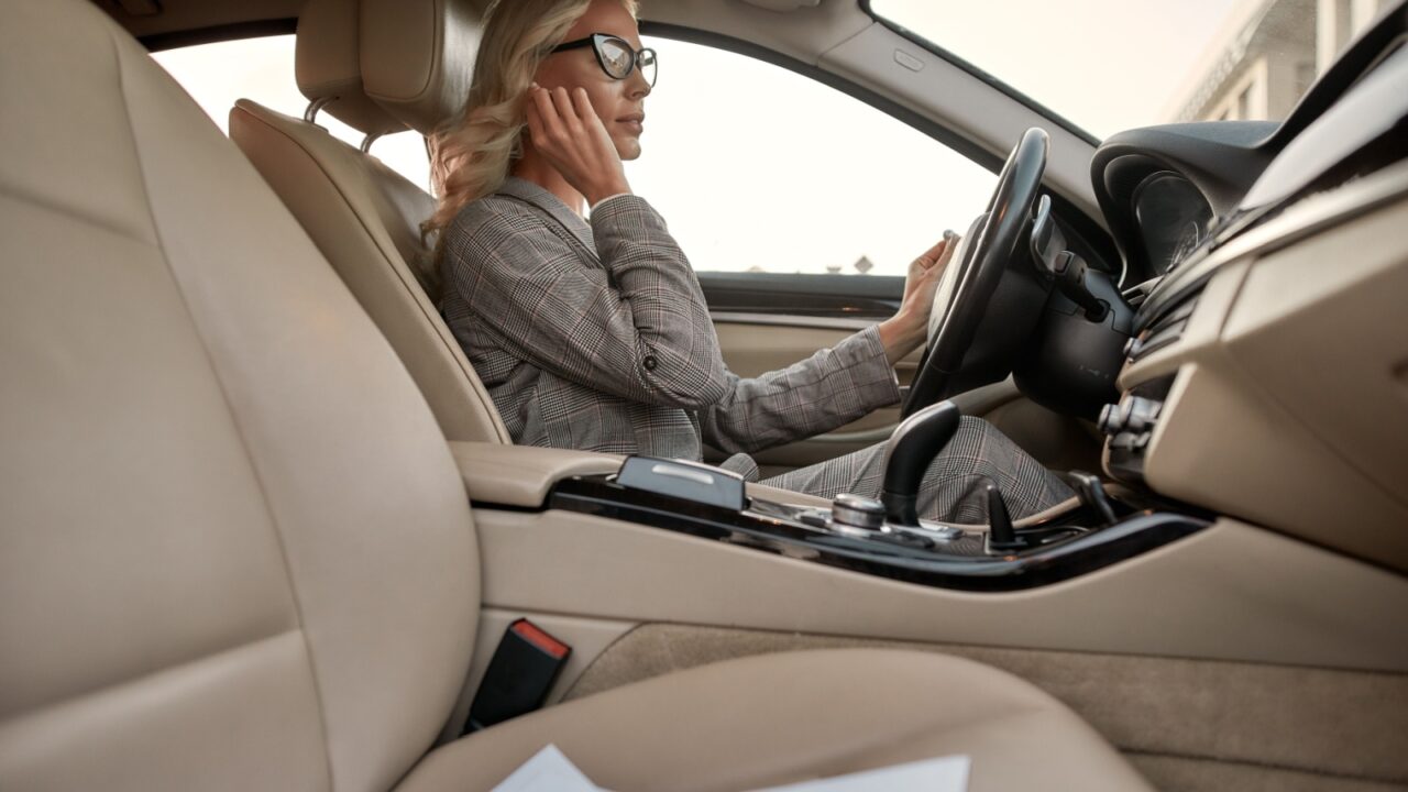 Listening music. Attractive and stylish businesswoman in classic wear adjusting headphones while driving a car. Business concept. Transportation. Driver