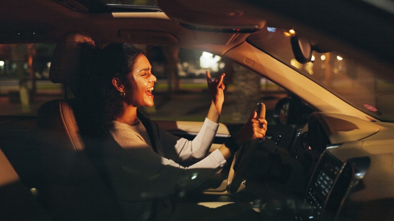 Singing, driving or happy woman in car at night, listening to radio or dancing for travel entertainment. Transport, music playlist or driver with sound system for fun, dark road or trip in vehicle