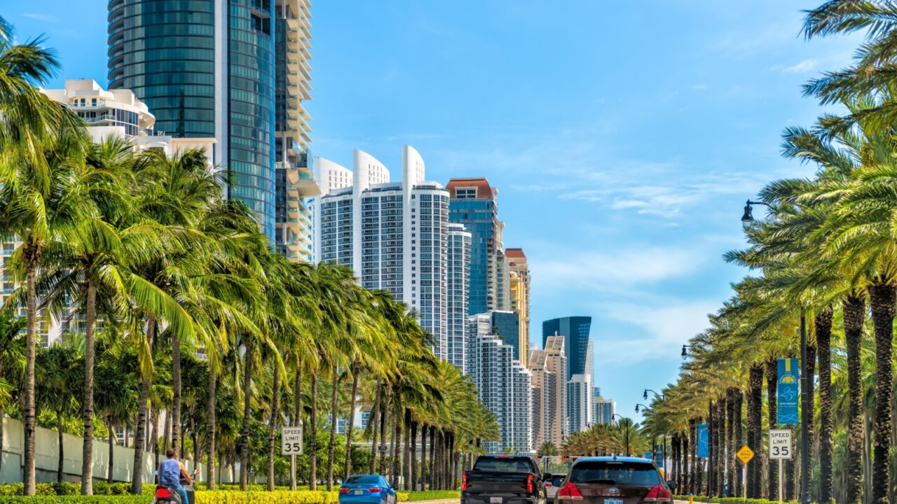 Sunny Isles Beach, USA - April 30, 2024: Florida road Collins Avenue street in Miami, Florida with cars by condo buildings and palm trees sunny day