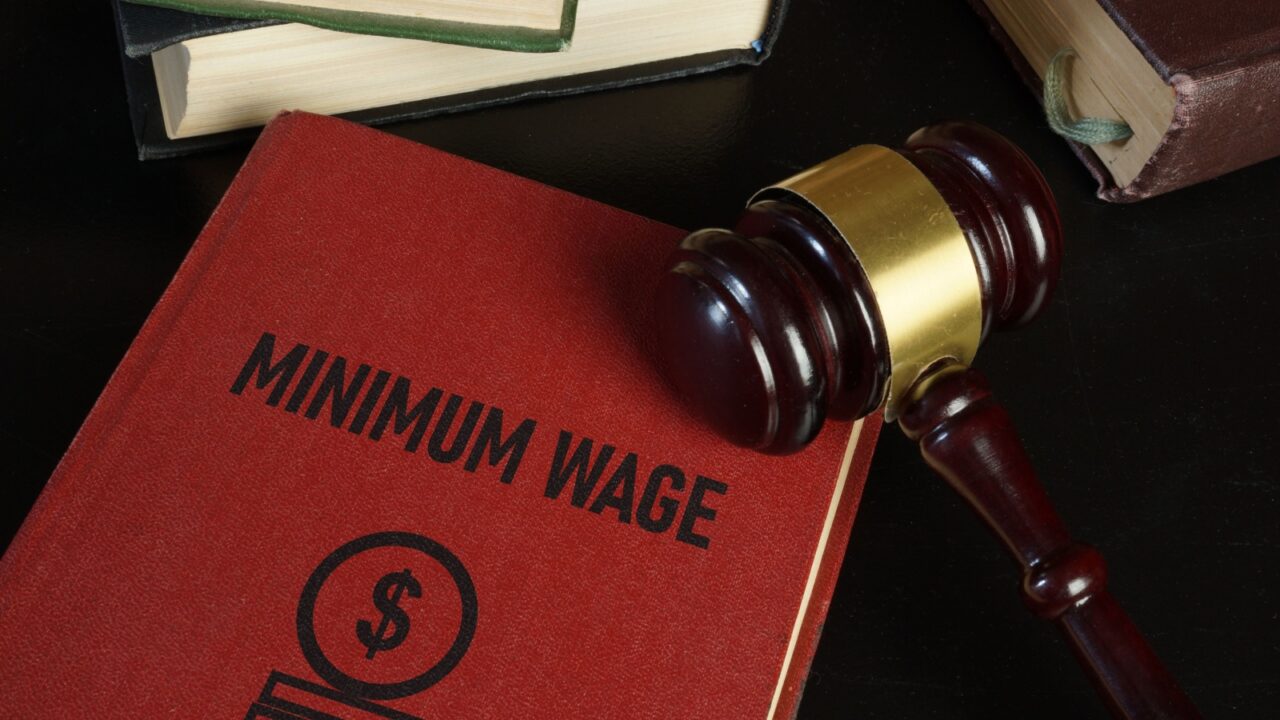 Minimum wage increase and minimum wage law are shown using a text on the book and photo of gavel