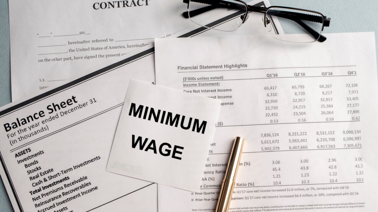 a paper with MINIMUM WAGE text on backgrounwith documents and glasses