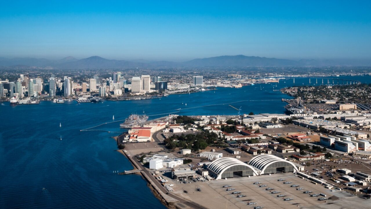 Aerial view of North Island Naval Air Base on Coronado and downtown San Diego California while flying over the bay with boats on the water and mountains in the background during daylight
