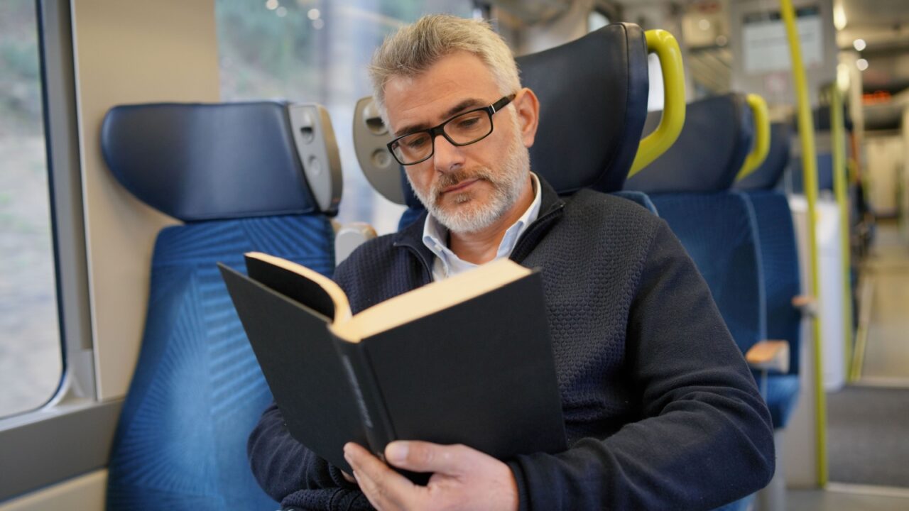 Mature man reading book while traveling on a train