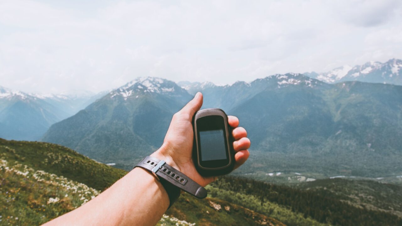 Traveler hand holding gps navigator tracker looking for location coordinates hiking in mountains Travel Lifestyle concept survival adventure summer vacations outdoor