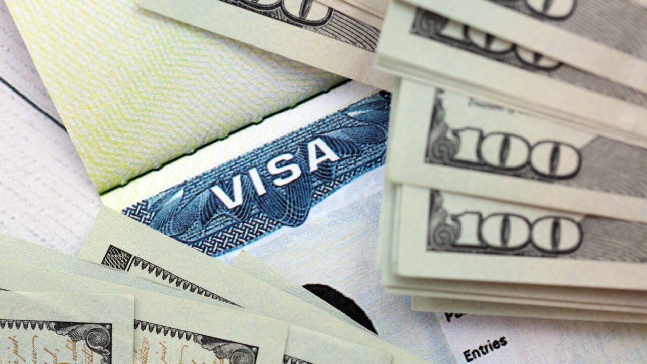 US visa sticker seen in passport and dollar banknotes placed on top. Concept for immigration and visa fees