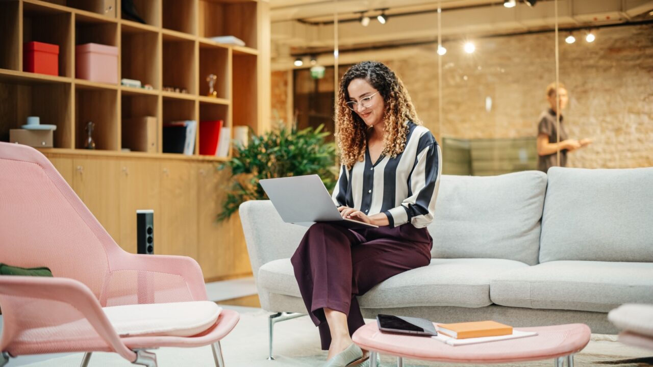 Portrait of Smiling Hispanic Woman Working on a Laptop in a Meeting Room at Office. Female Team Lead Smiling After Fulfilling an Important Task. E-commerce Specialist Researching on the Web
