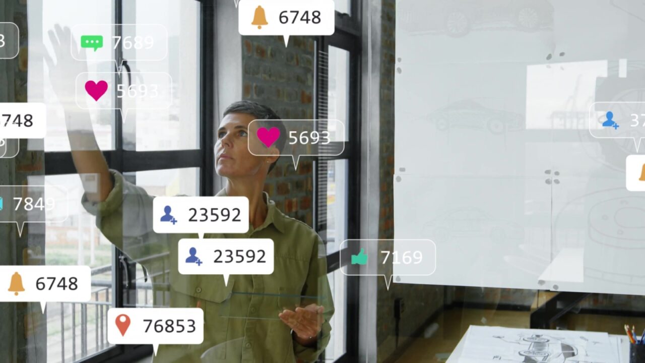 Woman in olive shirt tapping floating social media icons on glass wall in office, sketches, pencils. Modern, professional, minimalist, urban, technological, motivational, creative