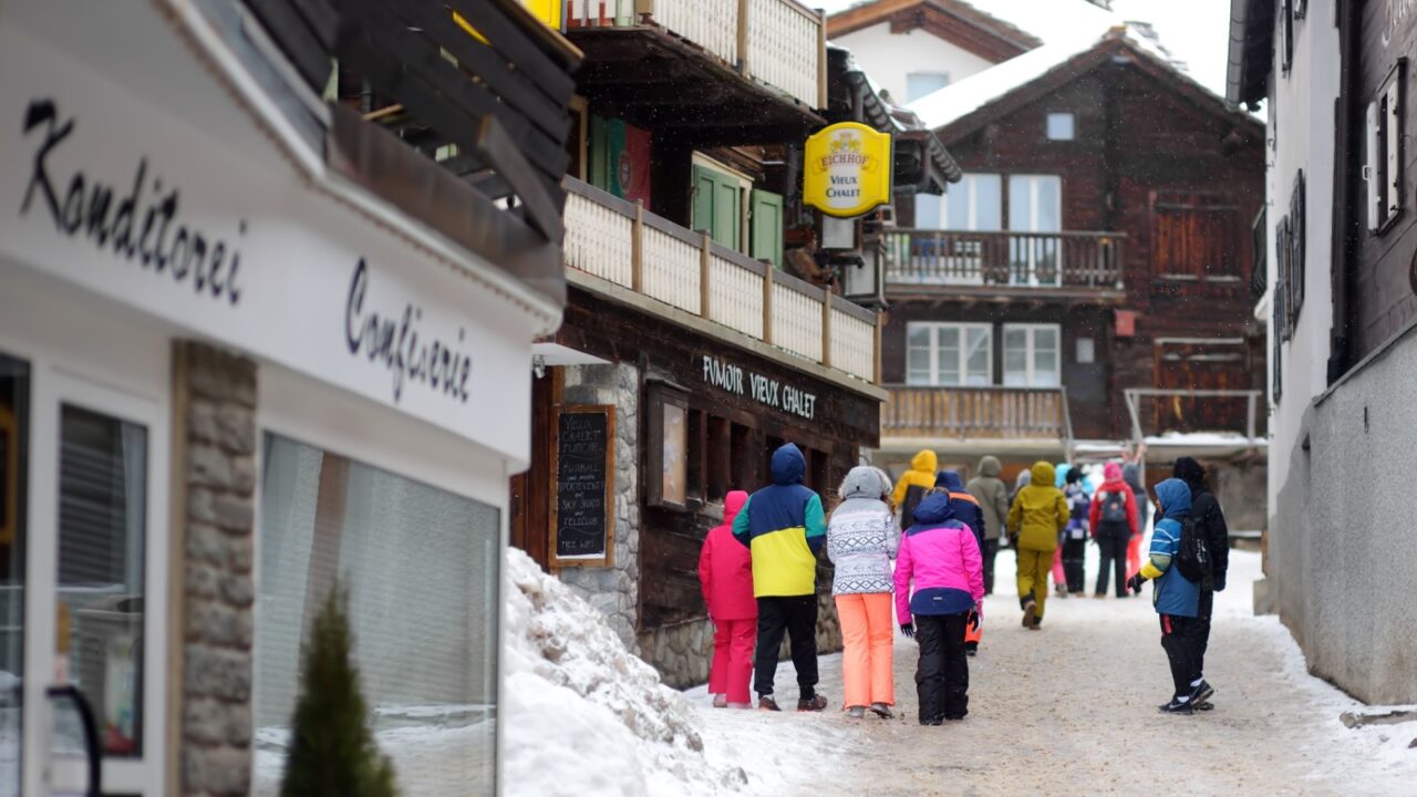 Saas Fee, Switzerland - February 4, 2020: Group of teenager tourists walking on street of mountain resort town in Switzerland, Europe. Winter vacation concept in Alps. Ski resort.