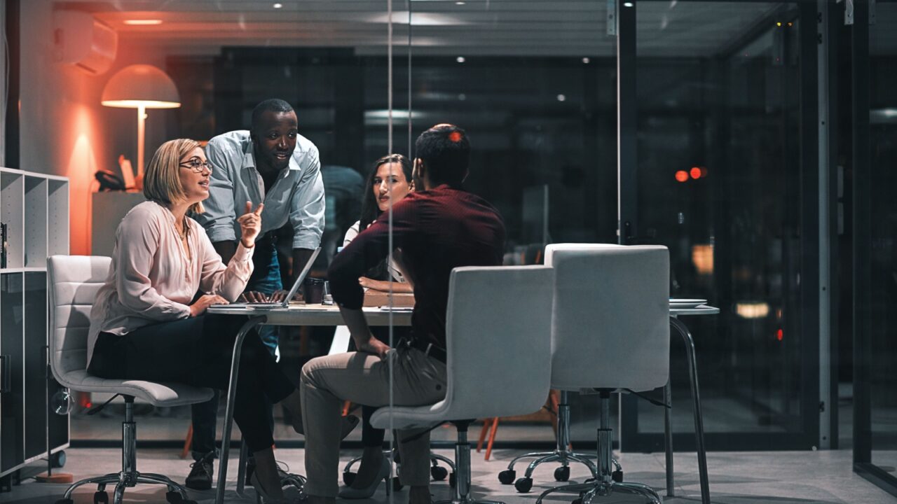 Business meeting, laptop and people for design at night in office, creative agency and overtime food for project. Teamwork, support and problem solving in pizza planning for deadline and discussion
