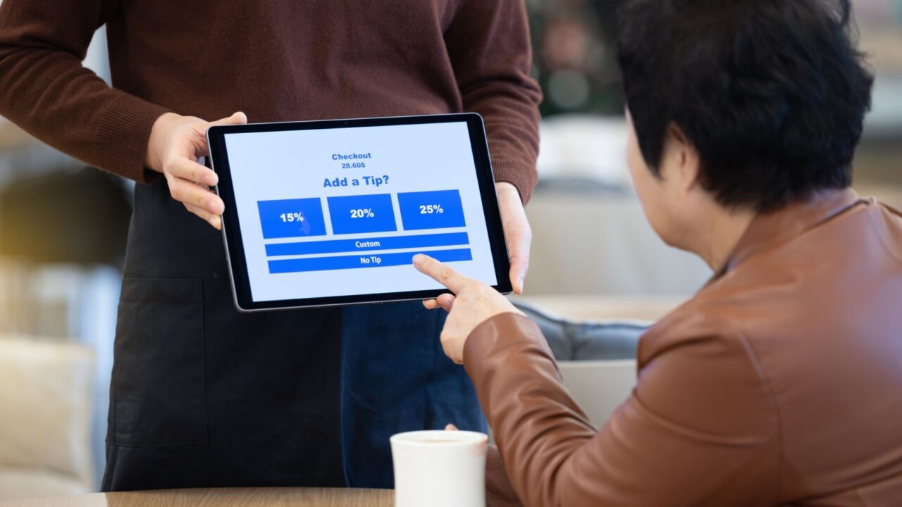 Employee holding tablet for tip payment in cafe and customer touching it to pay tip