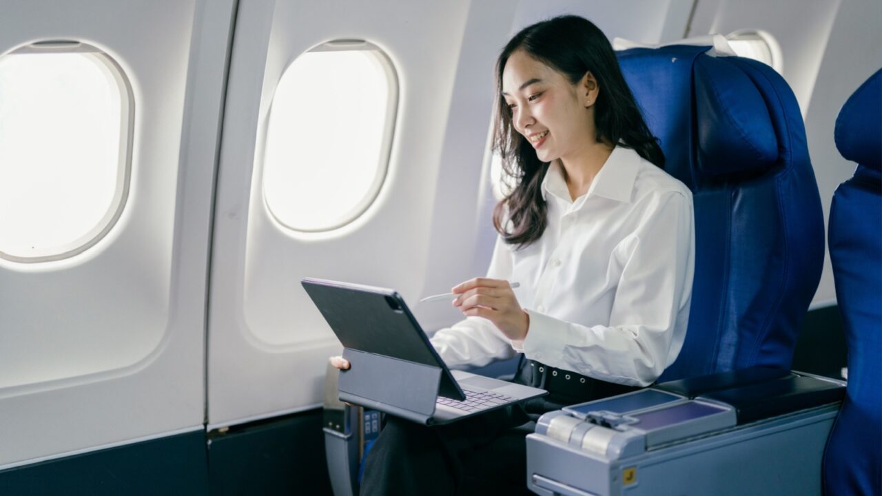 Professional woman using a tablet while traveling on an airplane, seated in a comfortable business class seat.