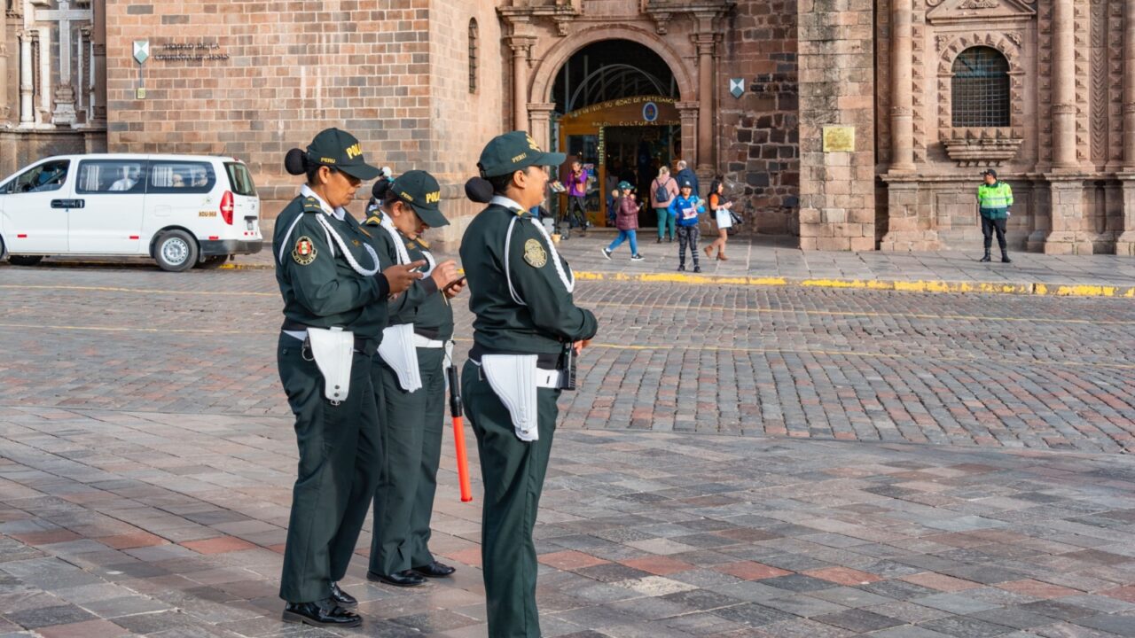 Three female Peruvian National Police officers in uniforms on patrol in the historic Plaza de Armas of Cusco.
