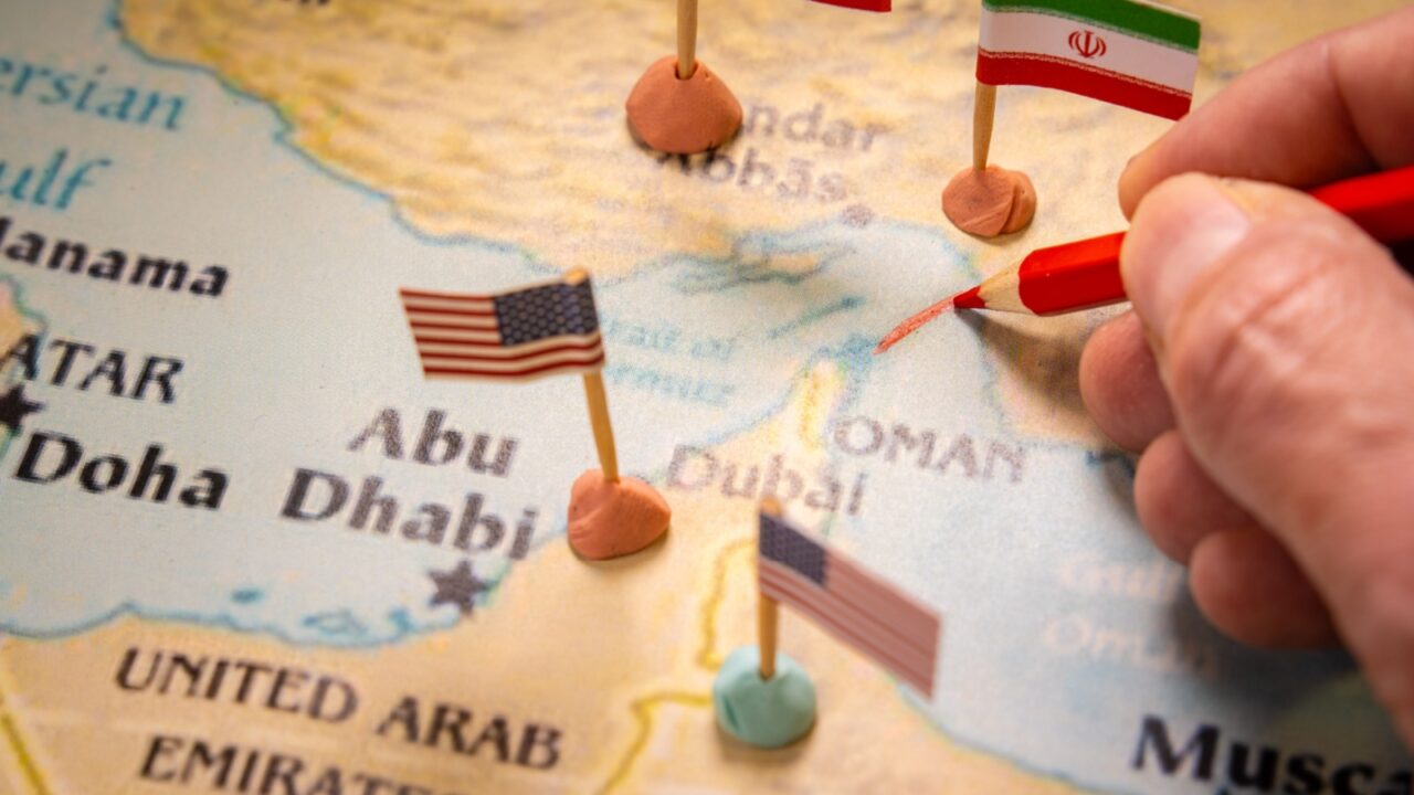 Conceptual image of a hand drawing a red line on a map of the Middle East with United States and Iran flags marking the Strait of Hormuz