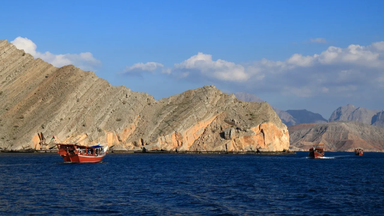 a vibrant red traditional dhow boat cruises on dark blue
