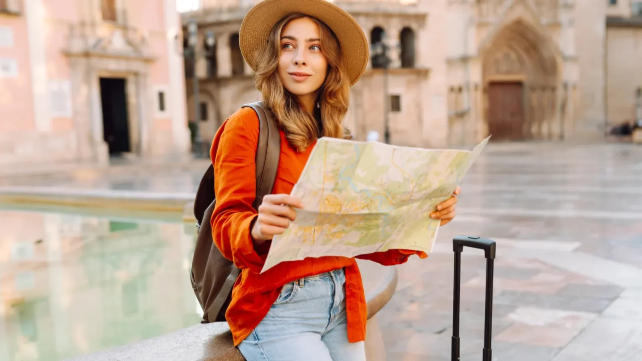 beautiful tourist in hat and carrying bright suitcase stands with
