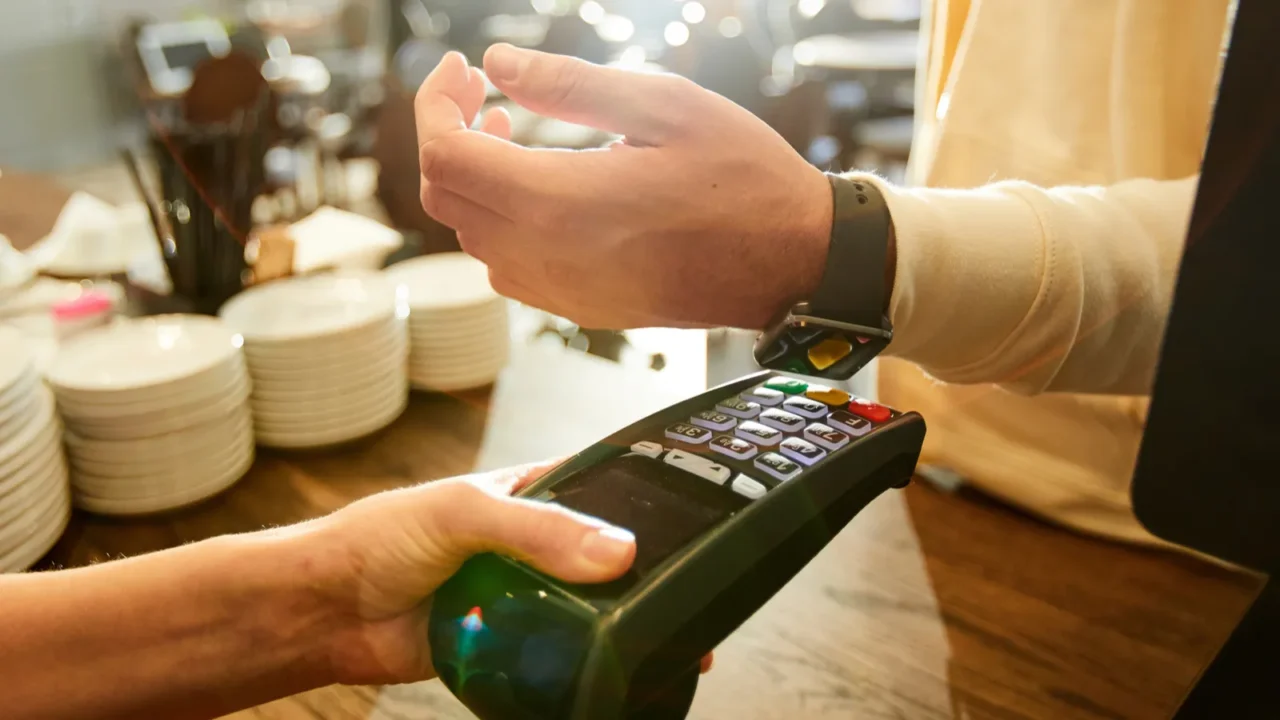 cashier holding payment machine while one of clients with smartwatch
