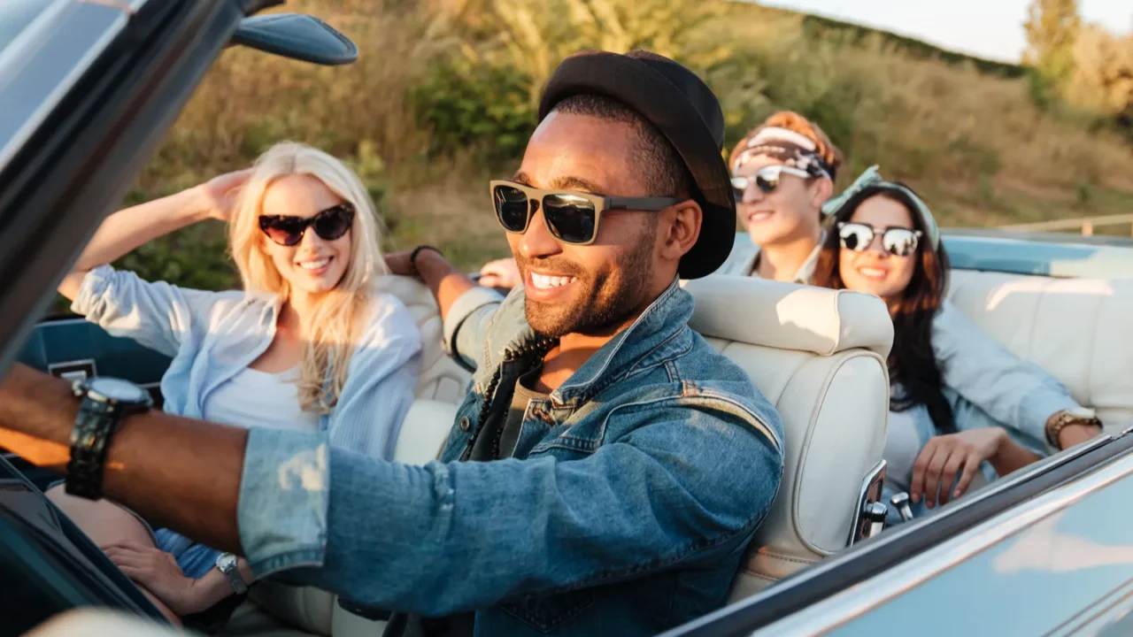 cheerful young friends driving car and smiling in summer