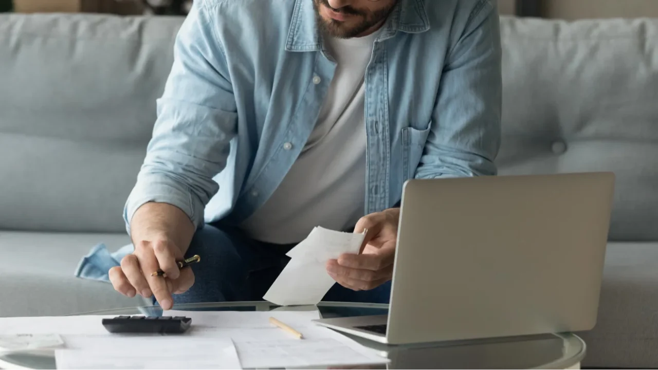 concentrated young 30s man in eyeglasses calculating expenditures