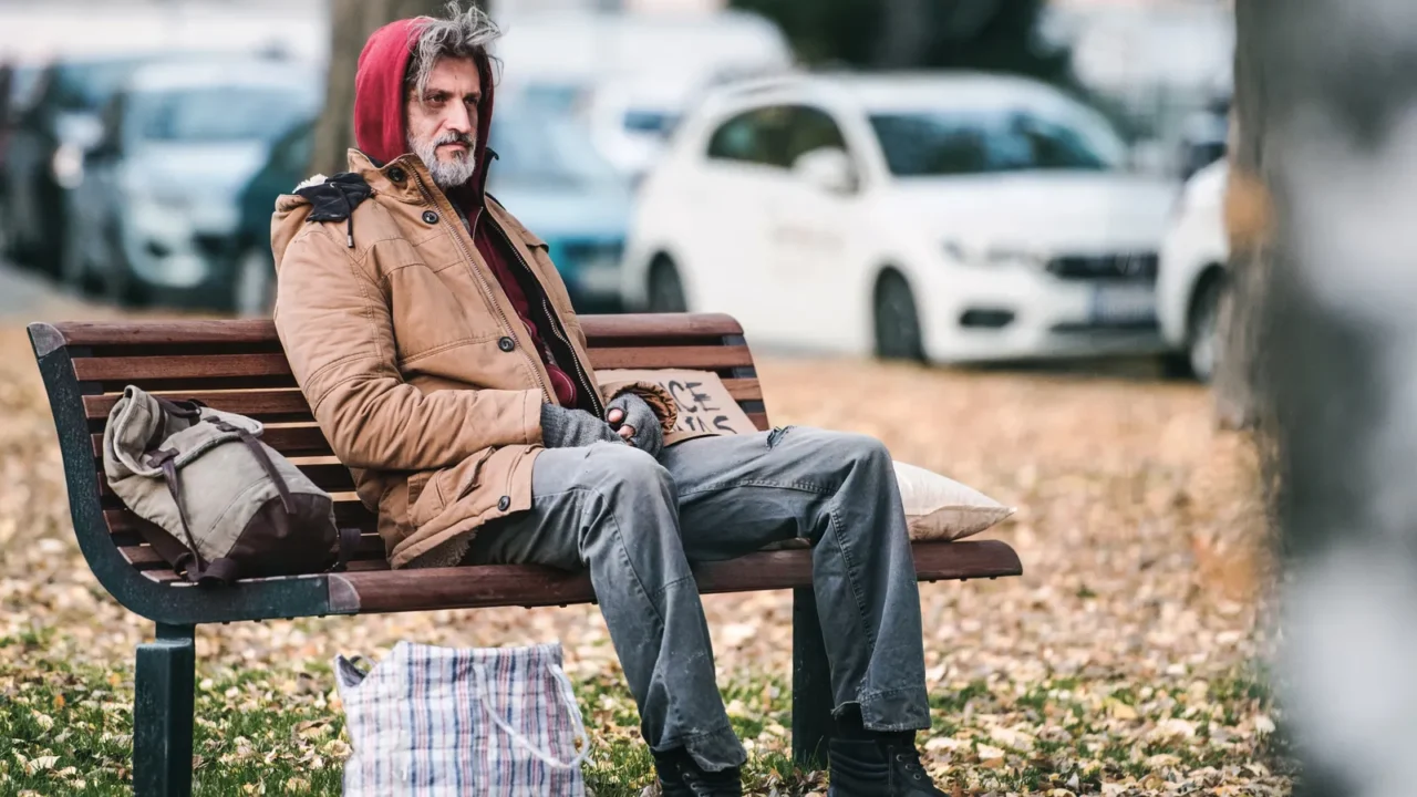 homeless beggar man with a bag sitting on bench outdoors