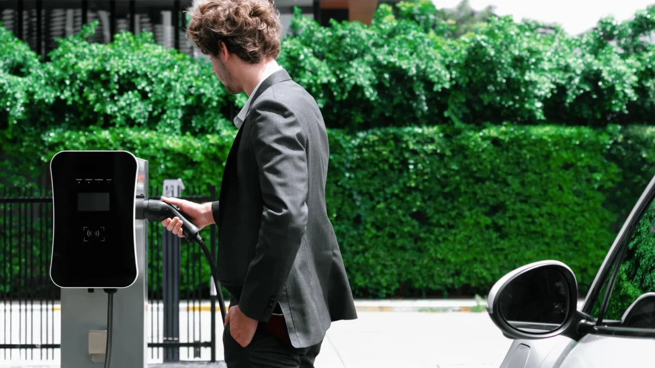 progressive businessman with electric car recharging at public charging station