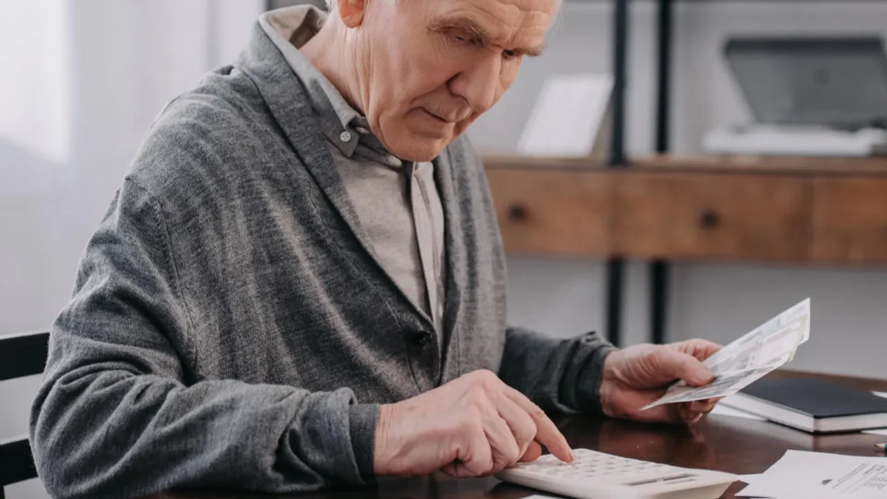 senior man sitting at table with paperwork and using calculator