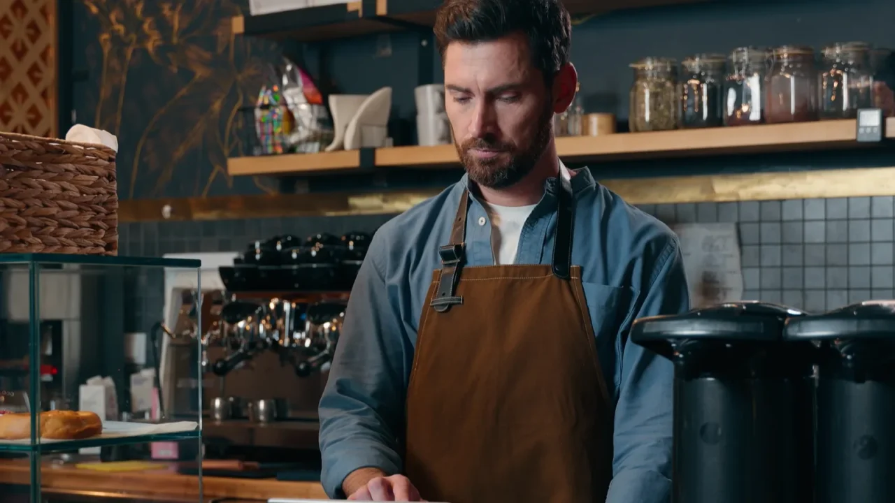 serious caucasian barista bartender male owner typing tablet in cafeteria