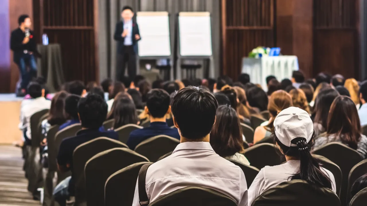 speaker on the stage with rear view of audience in