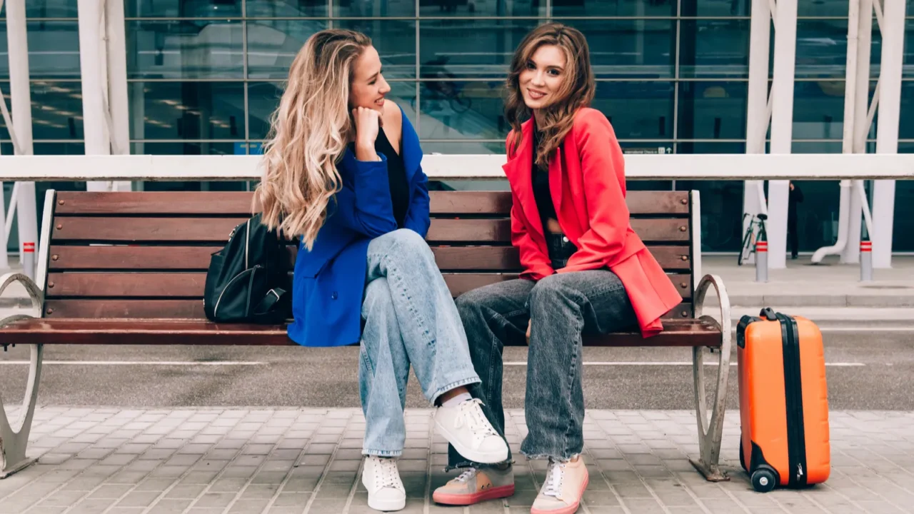 two happy girls sitting on a bench near airport with