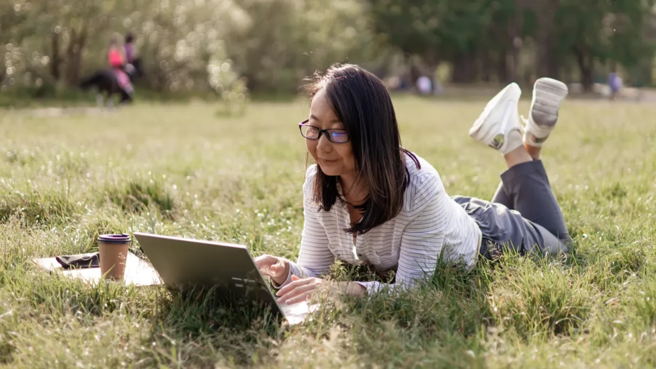 young asian woman with laptop sitting on green grass and