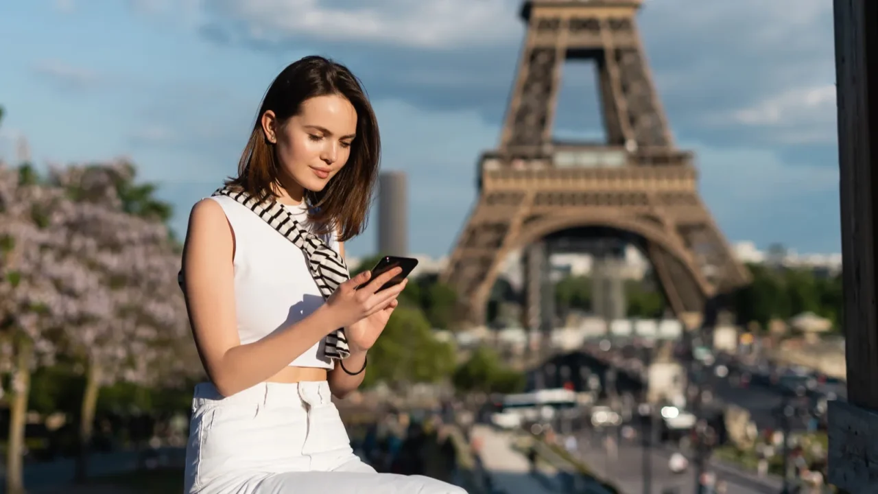 young woman in stylish outfit using smartphone while sitting near