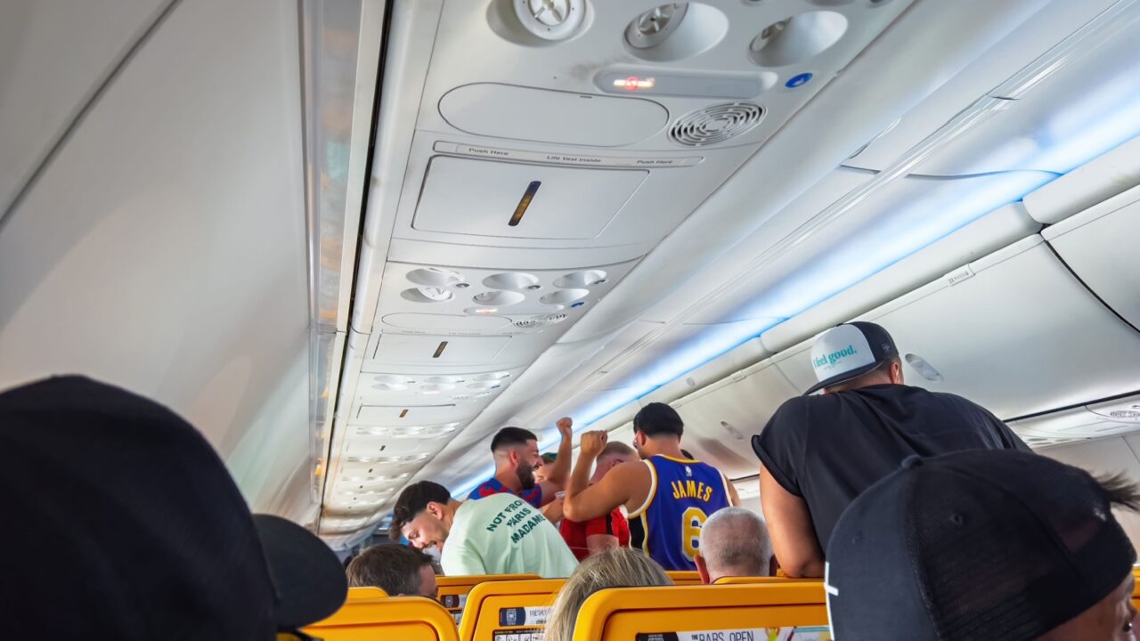 Berlin, Germany - Jun 22, 2023: boisterous German tourist in a basketball jersey and cap stands in the aisle of a crowded Ryanair cabin shouting into a cellphone as fellow vacation travelers glare