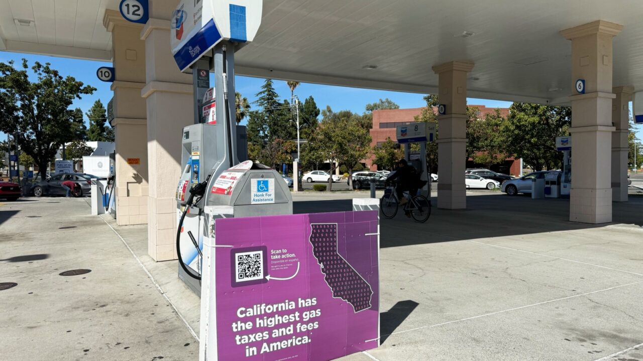 Chevron self-service gas station with sign reading "California has the highest gas taxes and fees in America", cyclist passing pumps - California, United States - October 17, 2025
